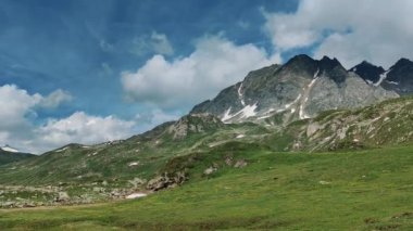Berrak mavi bir gökyüzünün altındaki dağlık bir çayırın manzarası. Bereketli yeşil çimenler ve engebeli dağ tepeleri. Arta kalan kar parçalarıyla bir yaz dağ manzarasının özünü yakalıyor.