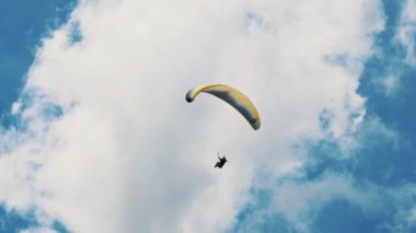 Özgürlüğün ve keşfin özünü bu çarpıcı paraglider görüntüsüyle yakalayın. Kabarık bulutlarla dolu canlı mavi gökyüzünde yükseliyor.