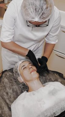 Beauty therapy. facial massage. Cosmetology skin care. beautician, in medical mask and gloves, performs cosmetic skincare facial scrubbing procedure, at beauty clinic. anti-aging. facial rejuvenation.