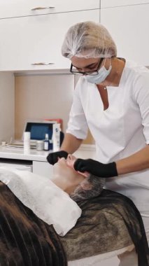 Güzellik terapisi. Kozmetik cilt bakımı. Kozmetik uzmanı, tıbbi maske ve eldivenlerle güzellik kliniğinde, kadın yüzünden ıslak mendillerle kozmetik cilt fırçası kalıntılarını çıkartıyor. Yaşlanma karşıtı. yüz gençleştirme.