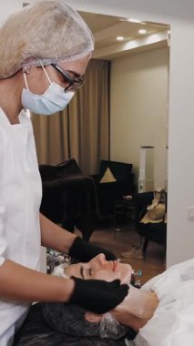 Beauty therapy. facial massage. Cosmetology skin care. beautician, in medical mask and gloves, performs facial skincare massage for woman, at beauty clinic. anti-aging procedure. Facial rejuvenation.