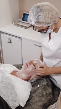 Yüz tazeleme. Doktor güzellik iğneleri yapmadan önce orta yaşlı kadın yüzüne anestezi kremi sürüyor. Yakın plan. Mezoterapi ve biyo-evitalleşme. Güzellik konsepti. Güzellik iğnesi. Yaşlanma önleyici enjeksiyonlar.