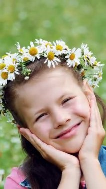 Papatya çimenlikte, tatlı bir kız gülümsüyor, papatyalar, çelenk içinde elleri onun yanakları için basarak