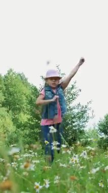 Çim, çayırda, dans, Zıplama, eğlenceli, güzel bir kız, yaklaşık yedi yaşında sahip papatyalar arasında. Uzun sarı saçlı, kot yelek ve pembe şapka giymiş