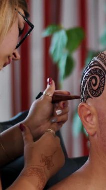 Bir kız dövme usta, kına dövmesi kel beyaz adam, omuz, boyun, kafa derisi üzerinde çizim mehendi sanatçı yapar. Ciltte kına kurur çözüm