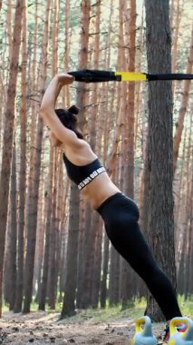 Atletik, eğitmen, egzersiz yapıyor, fitness sistemiyle egzersiz yapıyor, süspansiyon kayışları takıyor. Çam ormanlarında, yazın, güneş ışınlarında.