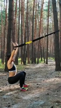 Atletik, eğitmen, egzersiz yapıyor, fitness sistemiyle egzersiz yapıyor, süspansiyon kayışları takıyor. Çam ormanlarında, yazın, güneş ışınlarında.