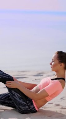 Sağlıklı, genç güzel kadın egzersiz kasları basına alır vücut, bacak, pompalar için sahilde kum güneş doğarken yatan basın gerçekleştirir.