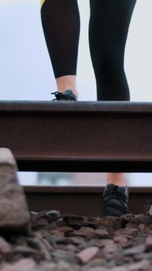 Siyah spor ayakkabılı ve taytlı kadın atletizm bacakları raylara atlıyor, yazın, demiryolunda. Dişi bacaklar için egzersiz yapıyor.,