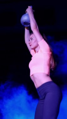 Ağırlıkları ile çeşitli güç egzersizleri yapıyor atletik, güzel genç bir kadın. Geceleri, projektörler, hangarda bir eski terk edilmiş, Bina hafif duman, sis ışığında.