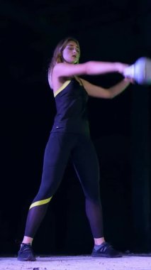 Ağırlıkları ile çeşitli güç egzersizleri yapıyor atletik, güzel genç bir kadın. Geceleri, projektörler, hangarda bir eski terk edilmiş, Bina hafif duman, sis ışığında