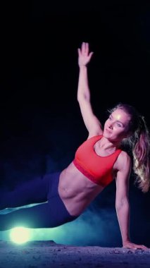 Atletik kadın spor yapıyor spor sistemi, süspansiyon kayışları. Geceleri, hafif dumanlarda, siste, çok renkli projektörlerde, terk edilmiş binada.