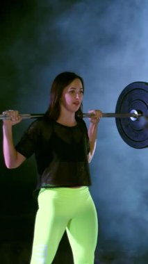 atletik genç kadın, halter yükseltir, halter ile mekik yok. Arkadan Görünüm. Geceleri projektörler, hafif duman, sis, bir eski terk edilmiş hangarda ışığında bina.