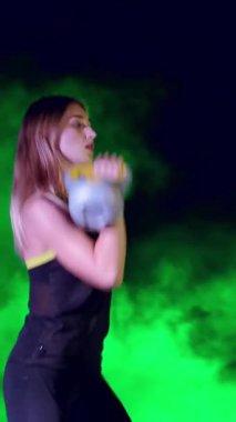 Ağırlıkları ile çeşitli güç egzersizleri yapıyor atletik, güzel genç bir kadın. Geceleri, projektörler, hangarda bir eski terk edilmiş, Bina hafif duman, sis ışığında.