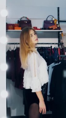 Dükkanda kıyafet deneyen ve aynanın karşısında kendine hayran olan bir iş kadını, gülümsüyor. Şık bir giyim mağazasından alışveriş yapmak. yavaş çekim