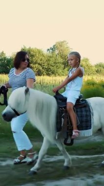 Kızı midilliye biniyor, annesi midilliyi dizginliyor. Neşeli, mutlu aile tatili. Açık havada, yazın, ormanın yakınında. Anne ve kızı tarlada yürüyorlar.