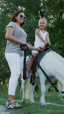 Kızı midilliye biniyor, annesi midilliyi dizginliyor. Neşeli, mutlu aile tatili. Açık havada, yazın, ormanın yakınında. Anne ve kızı tarlada yürüyorlar..