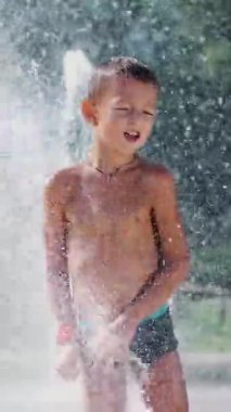 Sevimli çocuk, eğleniyor, yedi yaşında bir çocuk küveti bir çeşme ve oynarken su sıçrama içinde dışarıda, sıcak bir yaz günü. Ağır çekim.