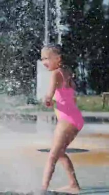 Mayolu bir kız, çeşmede yıkanan, etrafta koşuşturan, fışkırtan, eğlenen, sıcak bir yaz günü. Yavaş çekim