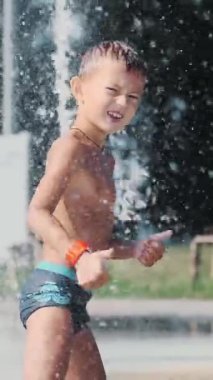 Yedi yaşında bir çocuk, sıcak bir yaz gününde çeşmede banyo yapıyor ve dışarıda su sıçratmaca oynuyor. Yavaş çekim