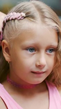 Yedi yaşında güzel sarışın bir kız, iki örgülü örgü örmüş, büyük bir aynanın önünde bir kuaför salonunda pembe bukleli saç stili yapmış. Küçük bir prenses.