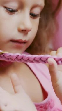 Yedi yaşında güzel sarışın bir kız, iki örgülü örgü örmüş, büyük bir aynanın önünde bir kuaför salonunda pembe bukleli saç stili yapmış. Küçük bir prenses.