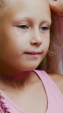 Yedi yaşında güzel sarışın bir kız, iki örgülü örgü örmüş, büyük bir aynanın önünde bir kuaför salonunda pembe bukleli saç stili yapmış. Küçük bir prenses.