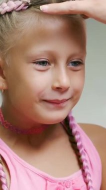 Yedi yaşında güzel sarışın bir kız, iki örgülü örgü örmüş, büyük bir aynanın önünde bir kuaför salonunda pembe bukleli saç stili yapmış. Küçük bir prenses.