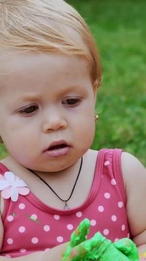 Küçük bir çocuk, oyun oynayan bir yaşında bir kız, parmak boyalarıyla resim yapan, kendini süsleyerek, bahçede, battaniyede, yatak örtüsünde, çimlerde, çimlerde, çimlerde, yazın. Eğleniyor..