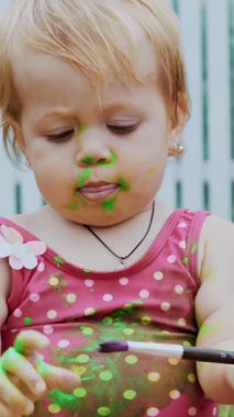 Küçük bir çocuk, oyun oynayan bir yaşında bir kız, parmak boyalarıyla resim yapan, kendini süsleyerek, bahçede, battaniyede, yatak örtüsünde, çimlerde, çimlerde, çimlerde, yazın. Eğleniyor.