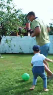Baba ve oğlu top oynuyorlar, futbol oynuyorlar, yeşil çimlerin üzerinde, yazın..