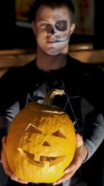 Cadılar Bayramı partisi, gece, ışık, adam kostümler giymiş bir kızla ve korkunç bir makyaj ile ışınları alacakaranlıkta tarzı tarihi olan holding iki büyük Halloween pumpkins
