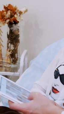Kozmetik uzmanı ve genç ve güzel bir hasta, tabletteki fotoğrafa bakarak dudak büyütme prosedürünü hyaluronik asitle tartışıyor. Klinik, kozmetoloji odası.