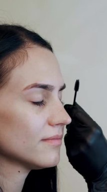 Siyah lastik eldivenli kozmetikçi özel bir fırça ve taraklı kaş tutuyor. Usta kaşların şeklini düzeltir. Profesyonel yüz bakımı.