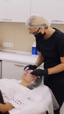 Kozmetik uzmanı, özel ıslak mendillerle kadın müşteri yüzünden kozmetik yüz ürününün kalıntılarını alıyor. Kozmetik kliniğinde veya güzellik salonunda cilt bakımı prosedürü.