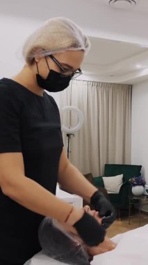 Maskeli ve eldivenli kozmetik uzmanı, cilt bakımı, kadınlara yüz masajı, kozmetoloji kliniği veya güzellik salonunda.
