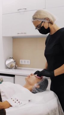 Kozmetik bilimci, maske ve eldiven takarak, özel ıslak mendilli kadın yüzünden kozmetik yüz ürününün kalıntılarını çıkarıyor. Kozmetik kliniğinde veya güzellik salonunda cilt bakımı prosedürü.
