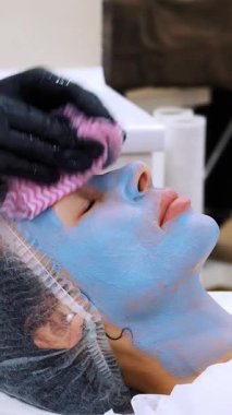 Siyah tıbbi eldivenlerle yakın plan kozmetik uzmanı, özel ıslak mendilli kadın yüzünden kozmetik maske kalıntılarını çıkarıyor. Kozmetik kliniğinde veya güzellik salonunda cilt bakımı prosedürü.
