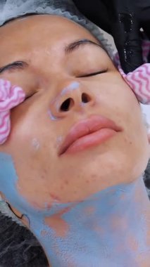 Siyah tıbbi eldivenlerle yakın plan kozmetik uzmanı, özel ıslak mendilli kadın yüzünden kozmetik maske kalıntılarını çıkarıyor. Kozmetik kliniğinde veya güzellik salonunda cilt bakımı prosedürü.