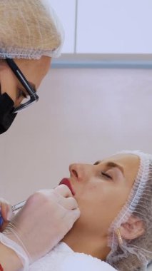 Dudak büyütme prosedürü. Cerrah, tıbbi eldiven ve maske ile kadının dudağına şırınga batırır ve yavaşça hyaluronik asit enjekte eder. Güzellik iğneleri. Estetik ameliyat.