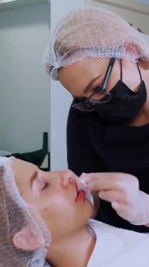 Dudak büyütme prosedürü. Cerrah, tıbbi maske ve eldivenlerle kadın dudaklarına masaj yaparak güzellik iğnelerinden sonra hyaluronik asit dağıtıyor. Estetik ameliyat.