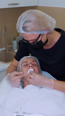 Dudak büyütme prosedürü. Cerrah, tıbbi maske ve eldivenlerle, güzellik iğnelerinden sonra kadın dudaklarına hyaluronik asit dağıtmak için masaj yapıyor. Estetik ameliyat.