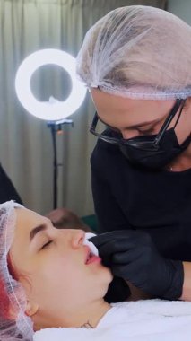 Dudak büyütme prosedürü. Cerrah, tıbbi eldivenlerle, dişinin dudaklarına masaj yaparak güzellik iğnelerinden sonra hyaluronik asit dağıtıyor. Estetik ameliyat.