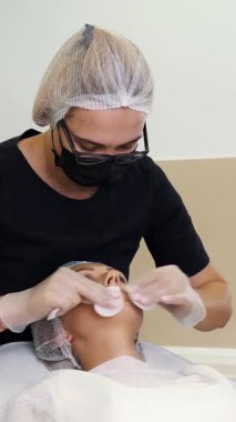 Kadın doktor, tıbbi eldiven ve maske ile kadın dudaklarını antiseptik ve anestetik solüsyonla siliyor. Pamuk pedleri, hyaluronik asit enjeksiyonlarıyla dudak büyütme prosedüründen önce..