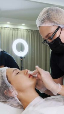 Dudak büyütme prosedürü. Cerrah, tıbbi maske ve eldivenlerle kadın dudaklarına masaj yaparak güzellik iğnelerinden sonra hyaluronik asit dağıtıyor. Estetik ameliyat.