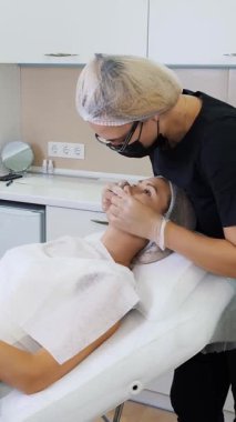 Dudak büyütme prosedürü. Cerrah, tıbbi maske ve eldivenlerle kadın dudaklarına masaj yaparak güzellik iğnelerinden sonra hyaluronik asit dağıtıyor. Estetik ameliyat.