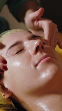 Yaşlanma önleyici prosedür, yüz masajı. Yakın plan. Kadın kanepede uzanıyor ve yüz masajı yaptırıyor. Güzellik kliniğinde yüz ve yüz derisi kanalizasyonu için. Cilt bakımı, kozmetoloji. Kadınlar için kozmetik prosedürleri.