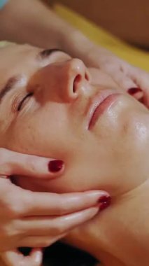 Yaşlanma önleyici prosedür, yüz masajı. Yakın plan. Kadın kanepede uzanıyor ve yüz masajı yaptırıyor. Güzellik kliniğinde yüz ve yüz derisi kanalizasyonu için. Cilt bakımı, kozmetoloji. Kadınlar için kozmetik prosedürleri.