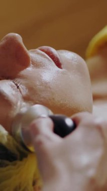 Kozmetoloji, yüz bakımı prosedürleri. Yakın plan. Bir kadının yüzünde altın aljinat kozmetik maske kullanma prosedürü. Yaşlanma karşıtı kozmetikler.