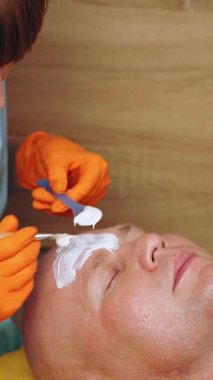 Kozmetoloji, yüz bakımı prosedürleri. Yakın plan. Bir kadının yüzünde altın aljinat kozmetik maske kullanma prosedürü. Yaşlanma karşıtı kozmetikler.
